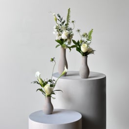 Three small white floral arrangements in matte vases on pedestals