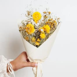 Handheld bouquet of yellow dried flowers wrapped in cream paper