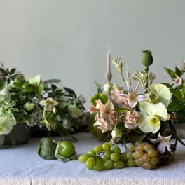 Floral arrangement with pale orchids and green grapes on a table