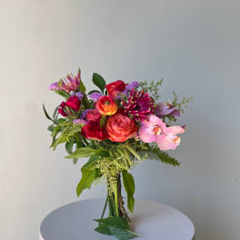 Mixed bouquet with roses, orchids, and purple accent flowers in a clear vase
