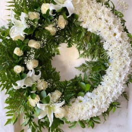 White floral wreath with lilies, roses, and daisies on a light background