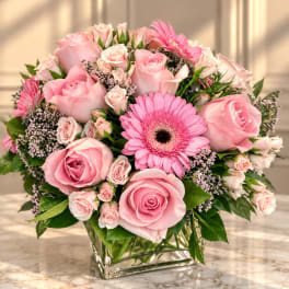 Pink roses and gerbera daisies arranged in a clear square vase