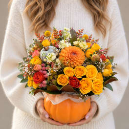 Autumn bouquet in a pumpkin container with yellow, orange, and red flowers
