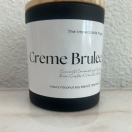 Black candle jar with a wood lid labeled Creme Brulee