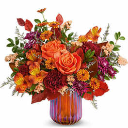 Orange roses and mixed fall flowers in a striped glass vase