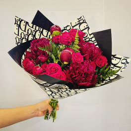 Handheld bouquet of hot pink roses and deep magenta blooms wrapped in black-and-white paper