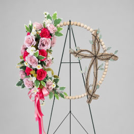 Floral cross wreath with pink roses and white daisies on a stand