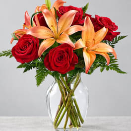 Red roses and peach lilies in a clear glass vase