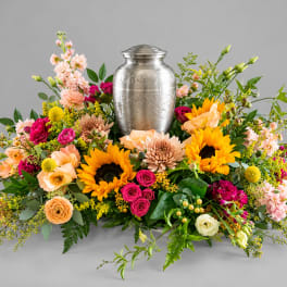 Colorful floral urn arrangement with sunflowers and roses around a silver urn