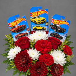 Red and white flowers in a red vase with Hot Wheels toy cars