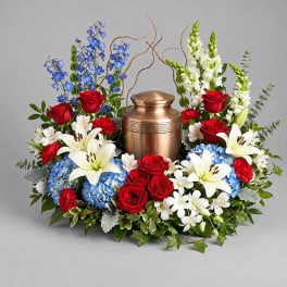 Floral funeral urn arrangement with red roses, white lilies, and blue flowers