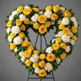 Heart-shaped floral wreath with yellow roses and white carnations on a stand