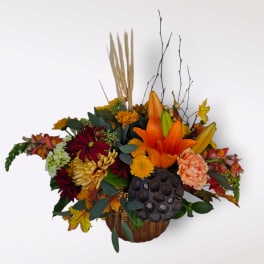 Autumn floral arrangement in a pumpkin-shaped container with orange lilies and chrysanthemums