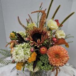 Mixed bouquet with a sunflower, dahlias, hydrangea, and calla lilies in a glass vase