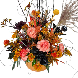 Autumn floral arrangement in a pumpkin-shaped container with pink and orange blooms