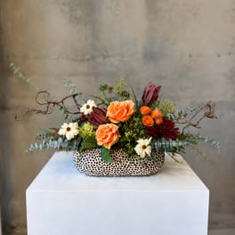 Orange and burgundy floral arrangement in a patterned low vase