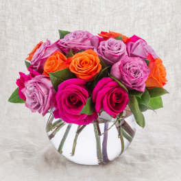 Mixed pink, lavender, and orange roses arranged in a clear glass vase.
