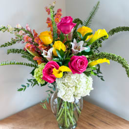 Bright mixed bouquet with pink roses, yellow calla lilies, and white hydrangeas in a glass vase
