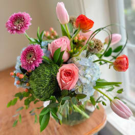 Mixed bouquet with pink roses, tulips, gerbera daisies, and blue hydrangeas in a glass vase