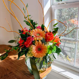 Orange and red mixed flower arrangement in a clear glass vase