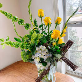 Yellow roses and white hydrangeas in a glass vase with a twig cross