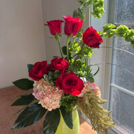 Red roses and pale hydrangeas in a lime-green vase by a window