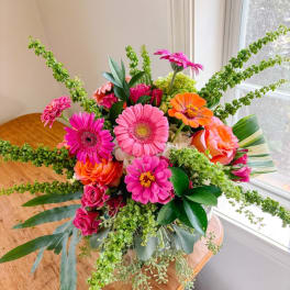 Bright mixed bouquet with pink gerberas, orange roses, and green filler in a vase