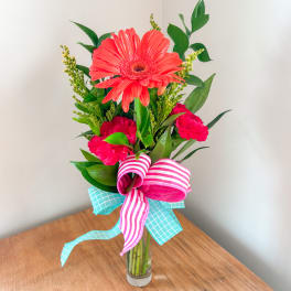 Pink gerbera and carnations in a clear glass vase with striped ribbon
