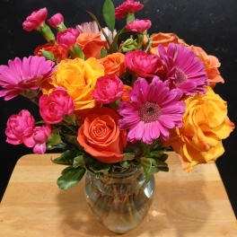 Mixed bouquet of pink, orange, and yellow flowers in a glass vase