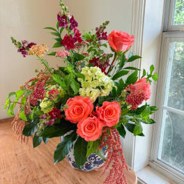 Mixed bouquet with coral roses, hydrangea, and snapdragons in a blue-and-white vase