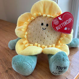 Plush sunflower toy with a red heart tag on a wooden surface