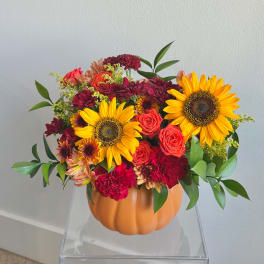 Sunflowers and mixed blooms arranged in a pumpkin-shaped container