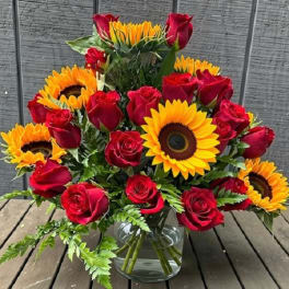 Red roses and sunflowers arranged in a clear glass vase
