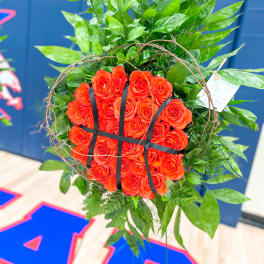 Orange roses arranged in a round wreath with green foliage