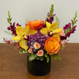 Orange roses and yellow orchids in a black vase with purple blooms