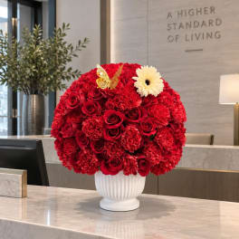 Round red floral arrangement in a white vase with a white daisy and butterfly accent