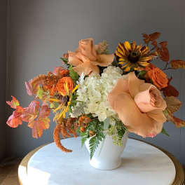 Peach roses and white hydrangeas in a white vase with autumn leaves