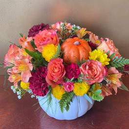 Mixed flower arrangement in a white pumpkin-shaped container with a small orange pumpkin centerpiece