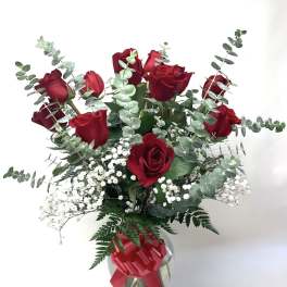 Red roses with baby's breath and eucalyptus in a glass vase with a red ribbon