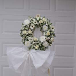 White floral wreath on a wooden easel with a large white bow