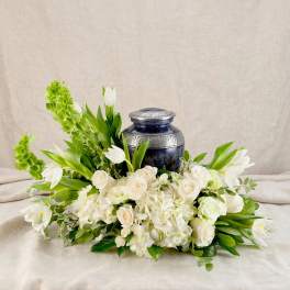White floral arrangement with roses and tulips around a dark blue urn