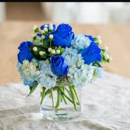Blue roses and pale hydrangeas in a clear glass vase