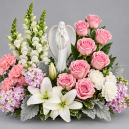 Pink roses and white lilies arranged around a white angel figurine