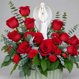 Red roses and carnations arranged around a white angel figurine in a vase