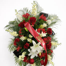 Standing funeral spray of red roses and white lilies with a red ribbon