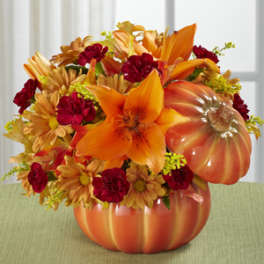 Orange and red floral arrangement in a pumpkin-shaped container