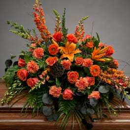 Orange floral casket spray with roses, lilies, and carnations