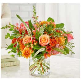 Mixed bouquet of peach roses and orange blooms in a clear glass vase