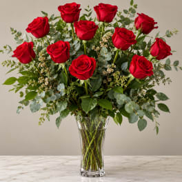 Red roses arranged in a clear glass vase with mixed greenery
