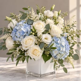 White roses and blue hydrangeas in a square glass vase
